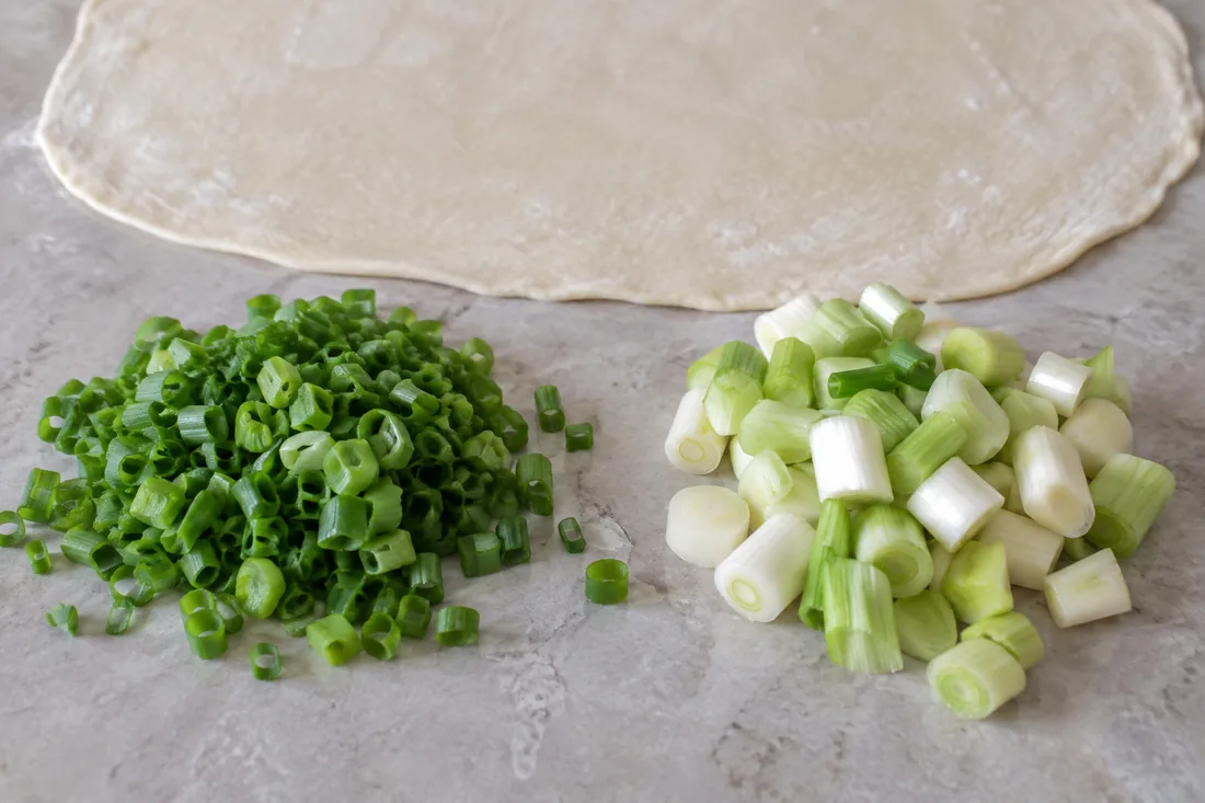 Two chopped spring onion cuts beside a thin dough sheet