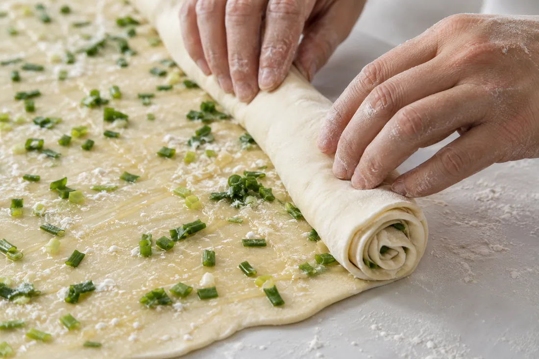 Hands shaping an oiled scallion pancake coil with visible thin layers